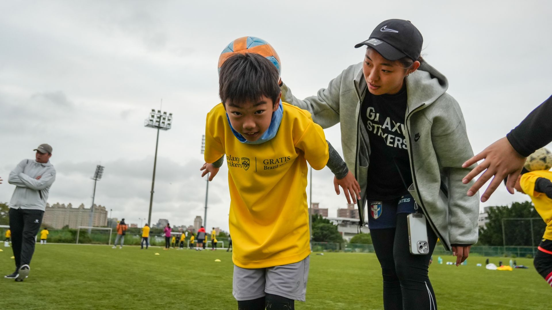 一名婦女正在球場上幫助一名小男孩踢足球。