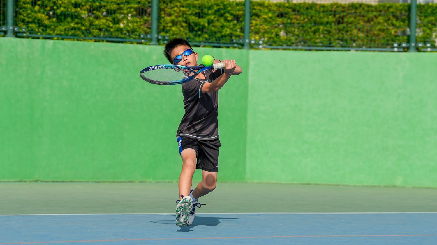 一個小男孩正在網球場上打網球。