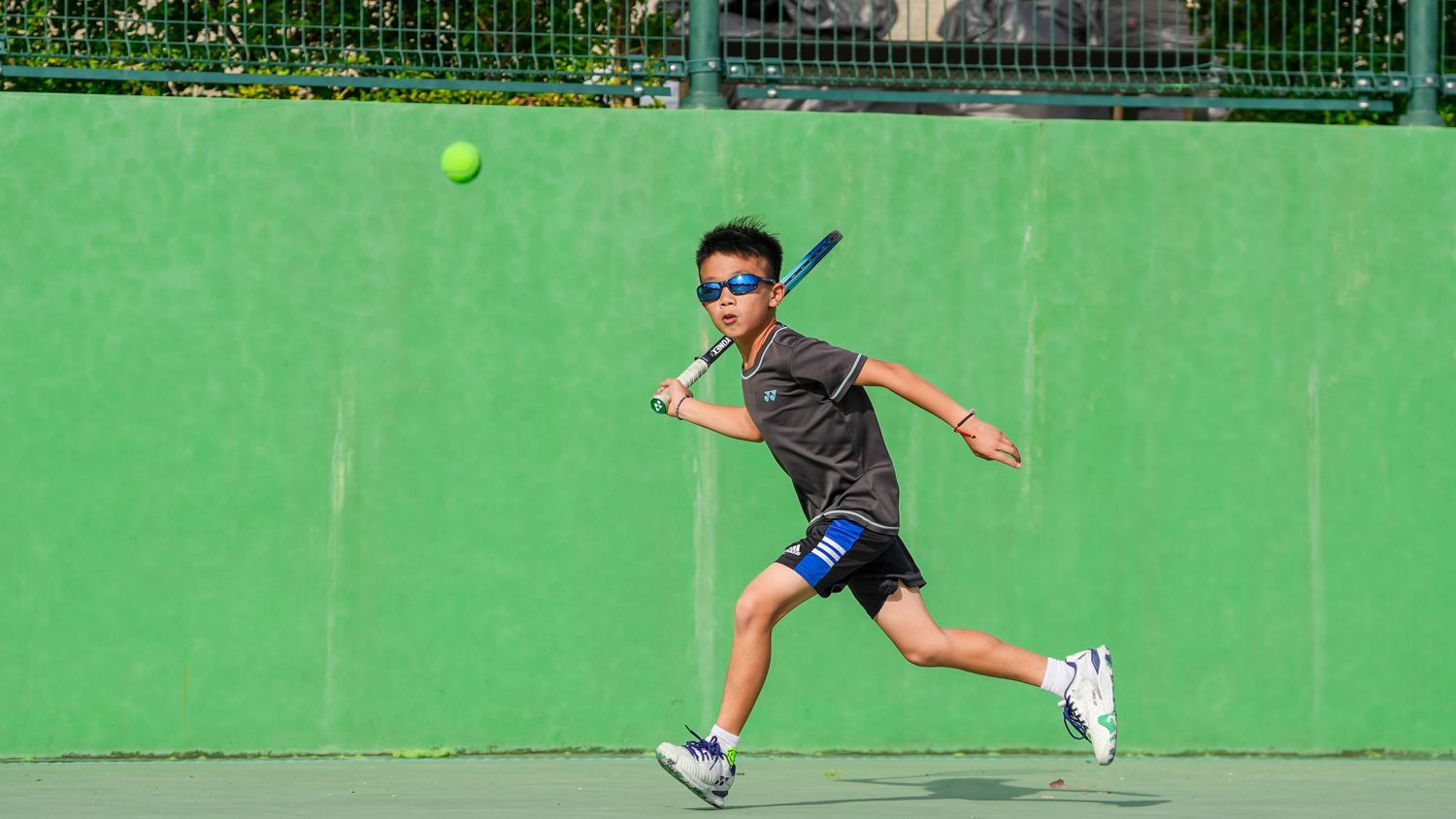 一個小男孩正在網球場上打網球。