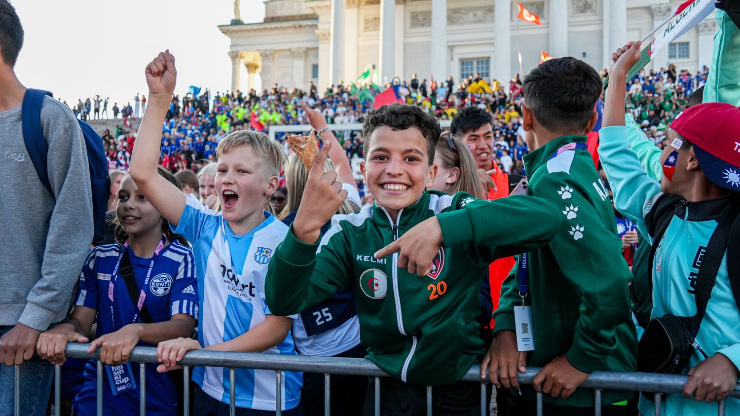 一群小男孩站在柵欄後面觀看足球比賽。