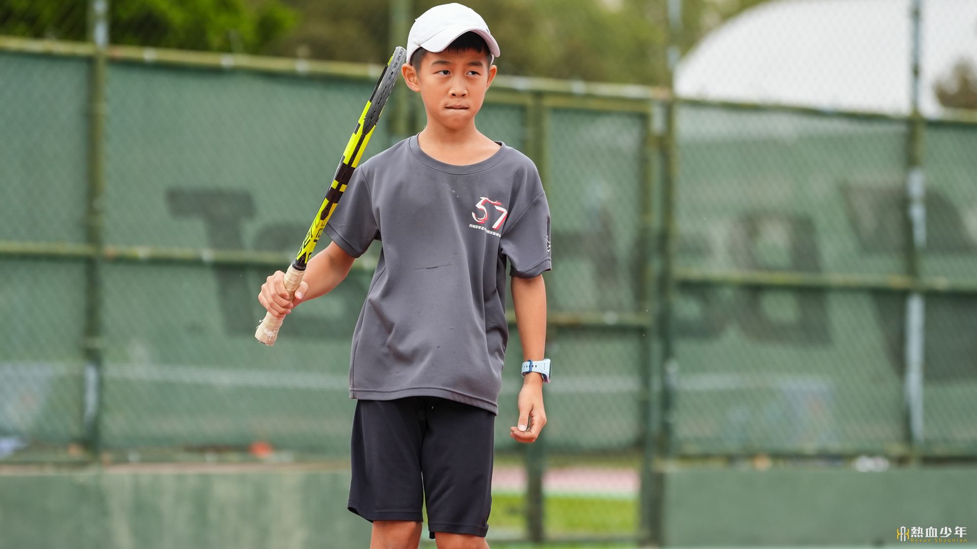 一個小男孩拿著網球拍在網球場上。