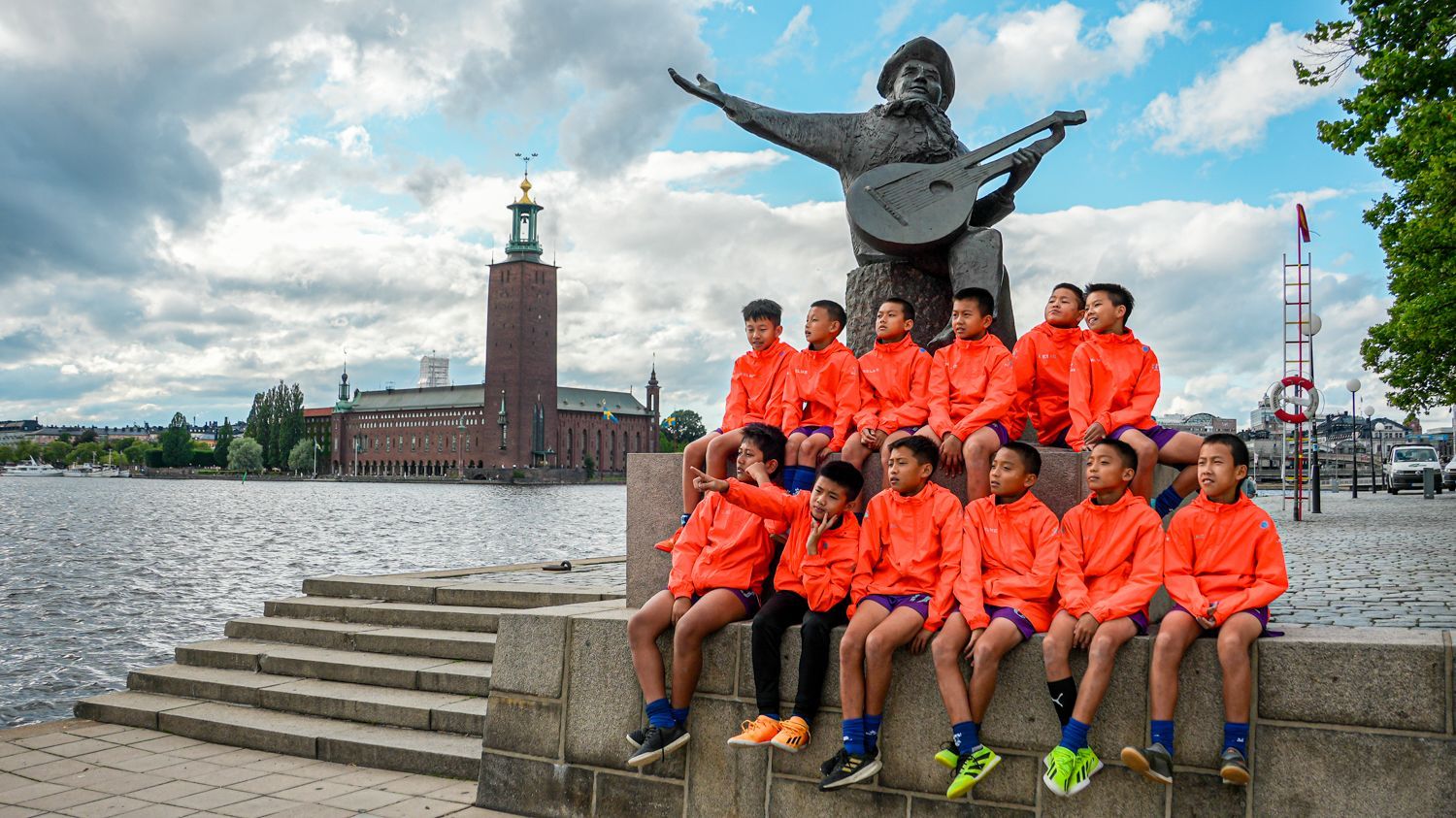 一群孩子坐在一個拿著吉他的男人雕像旁邊。