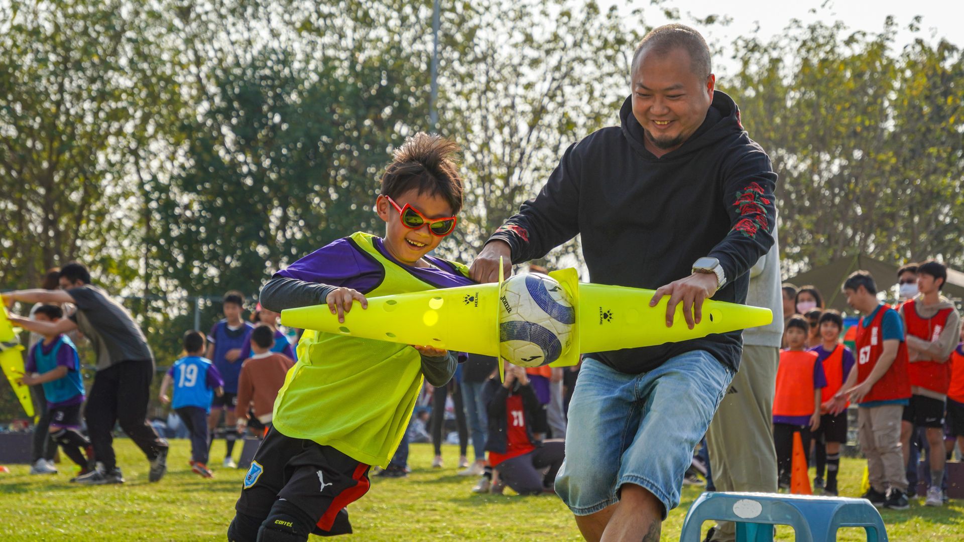 一個男人和一個男孩正在操場上玩圓錐形足球。