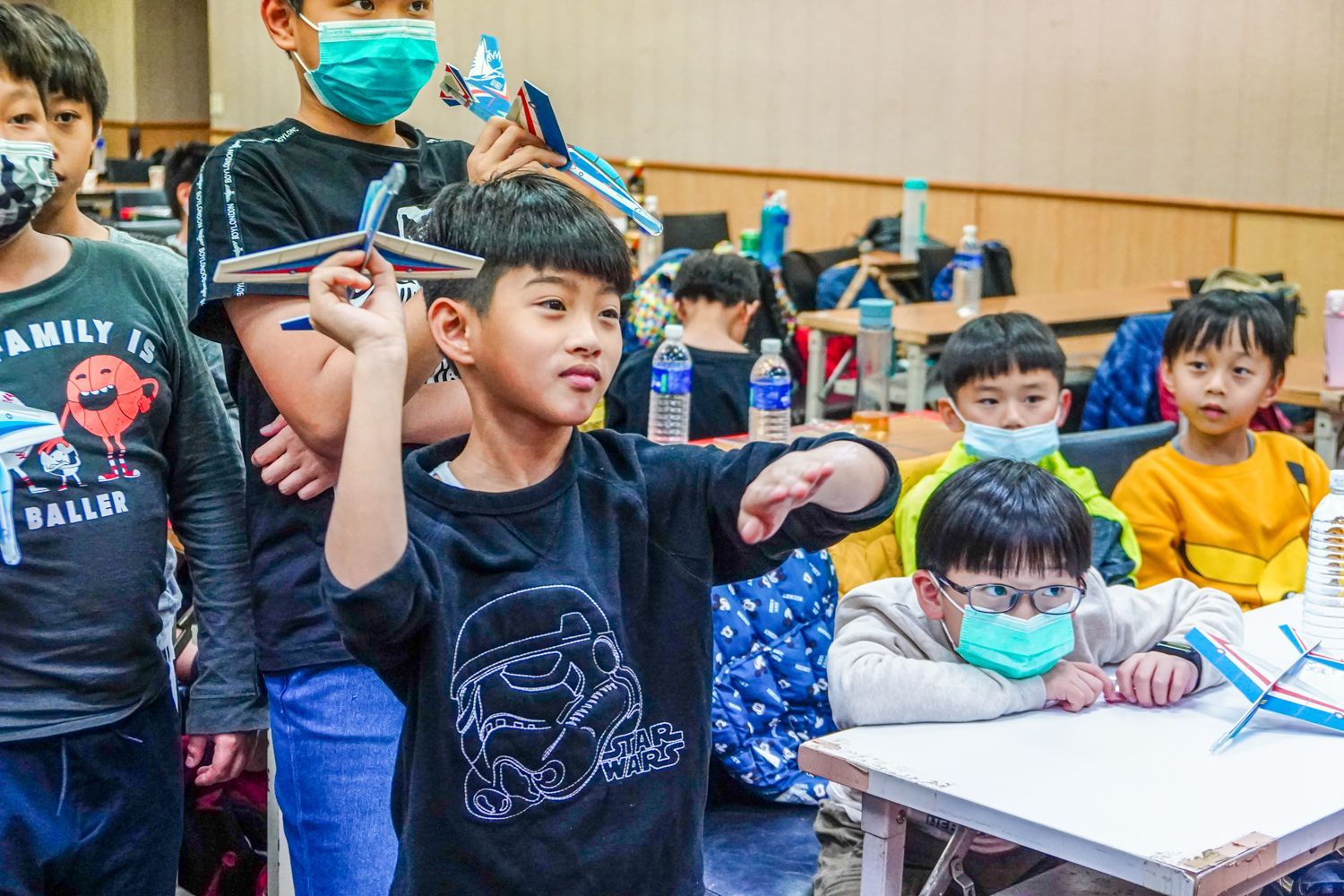一群戴著口罩的孩子在教室裡玩紙飛機。