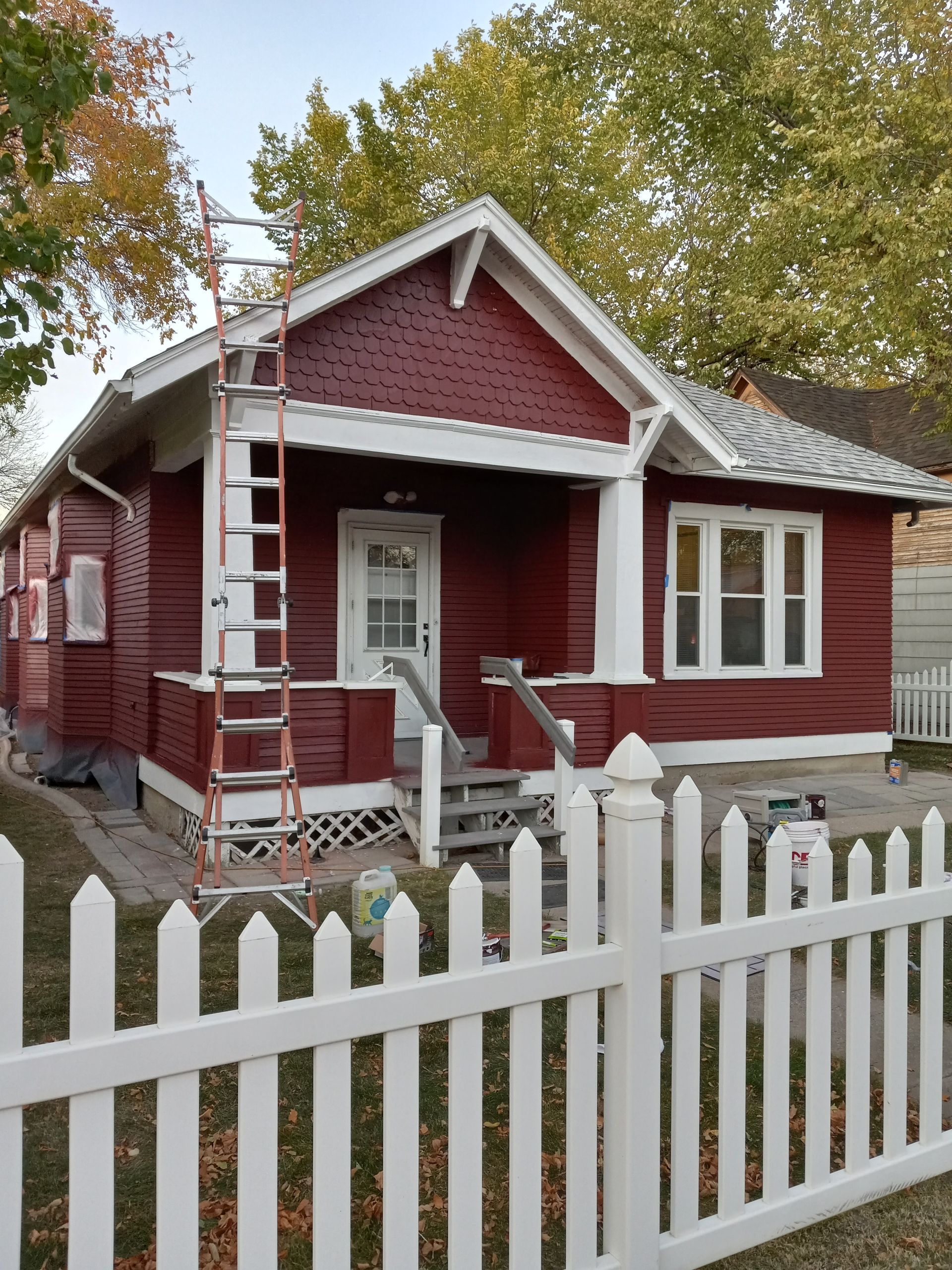 Red house with white trim and picket fence, ladder leaning against the porch.