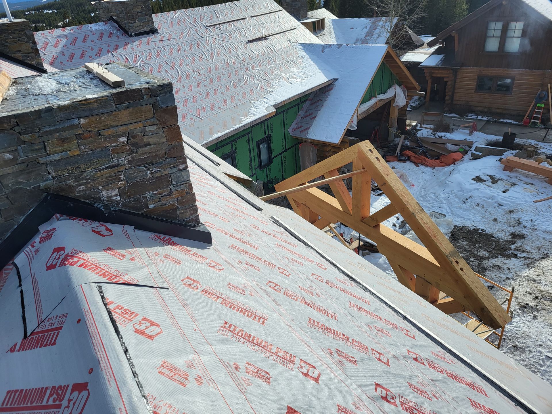 Construction site with a partially built roof covered in snow, showing wooden beams and other building materials.