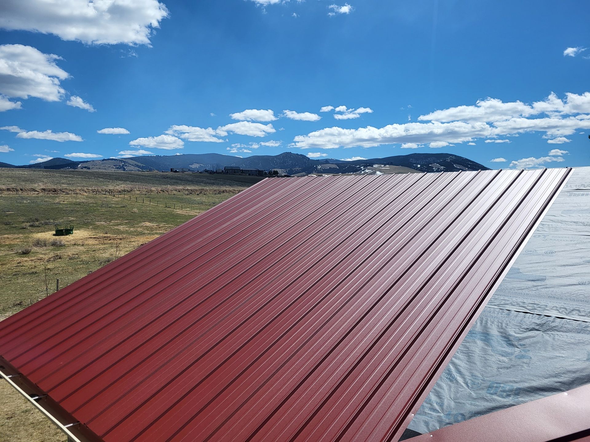 Red metal roof under a blue sky with clouds. Landscape in the background.