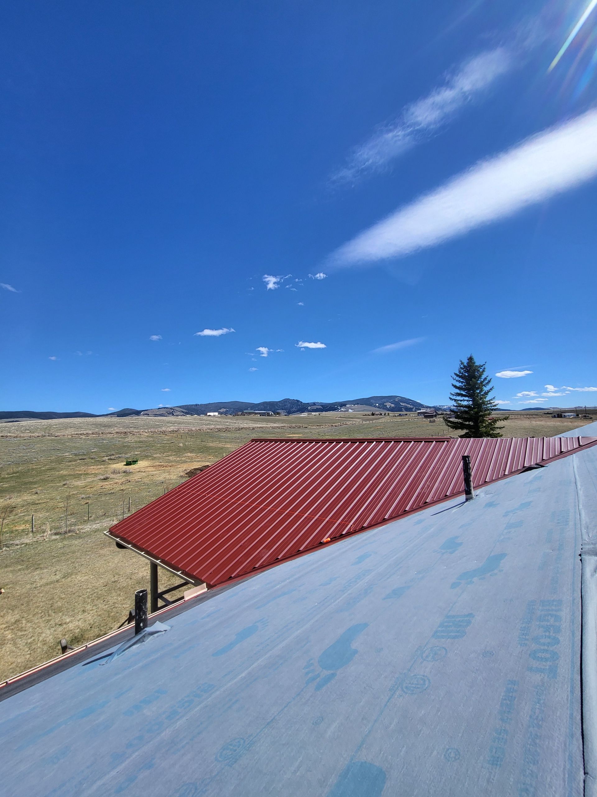 Red metal roof under a bright blue sky with sparse clouds and distant mountains.