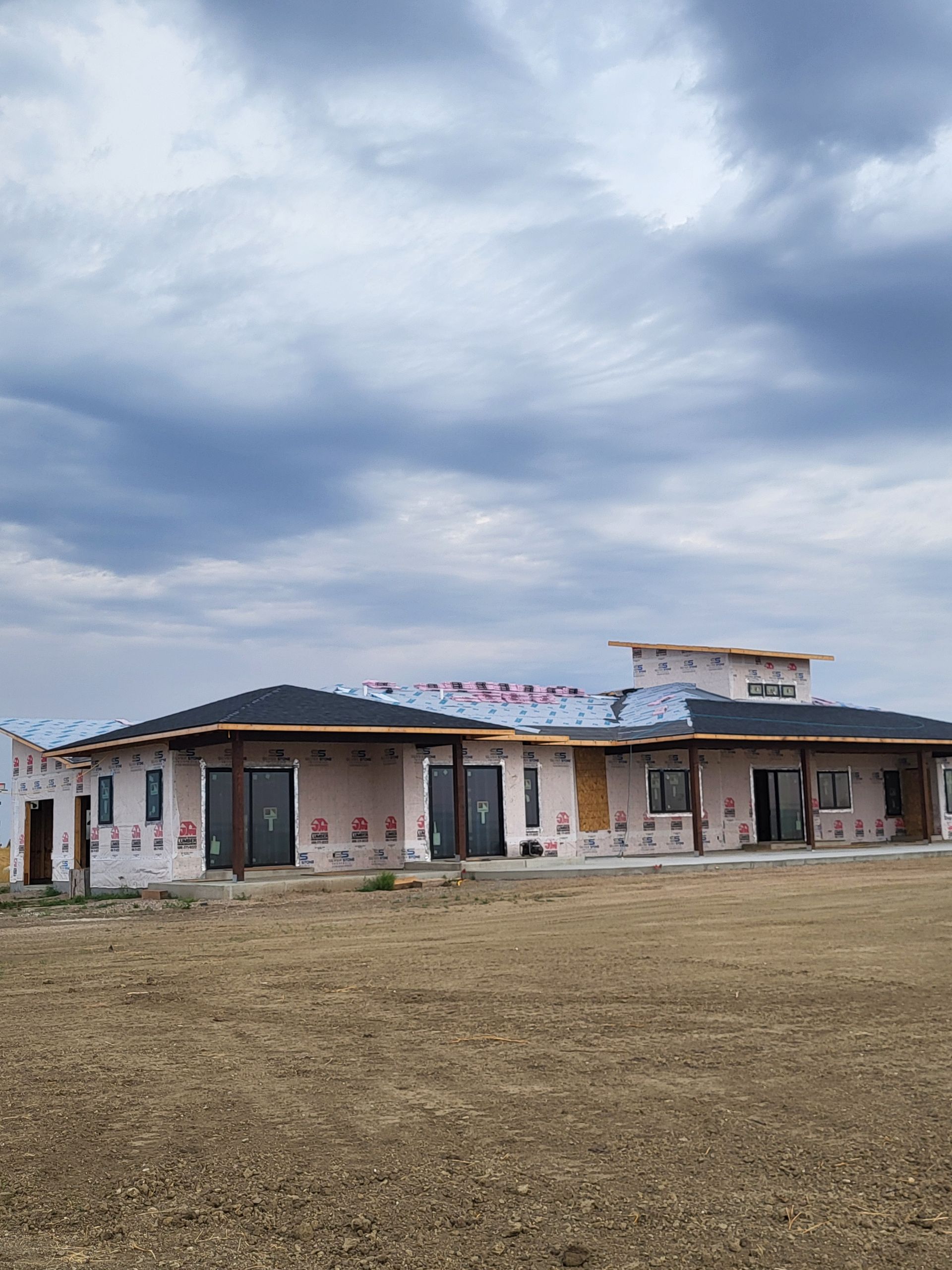 House under construction with exposed sheathing, windows, and partial roof; outdoors under cloudy sky.
