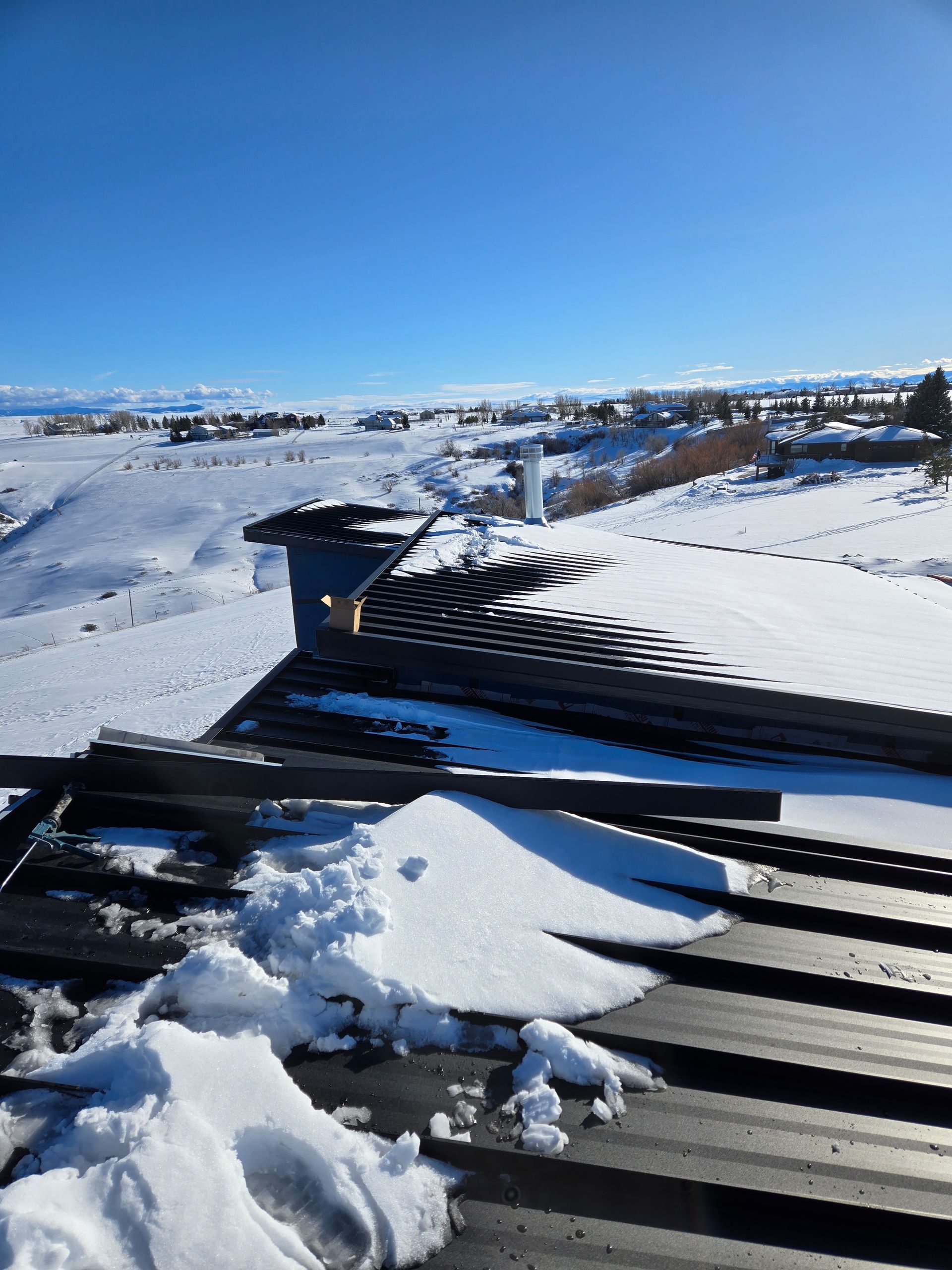 Snow-covered metal roof, landscape with snow, blue sky.