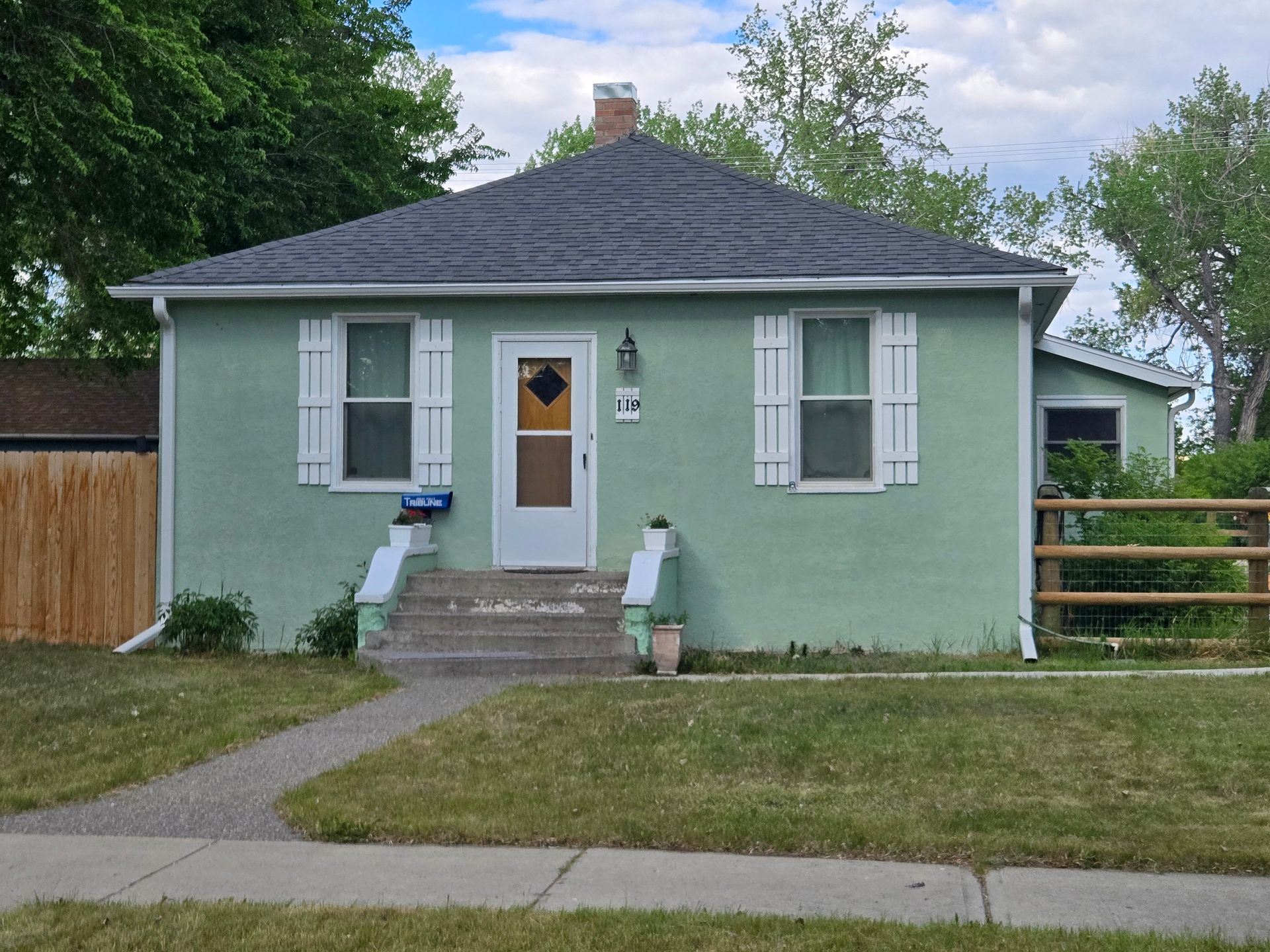 Green stucco house with white shutters, door, and stairs leading to the entrance. Dark roof.