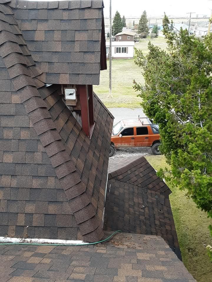 Brown shingled roofs of a building, with an orange truck and green trees in the background.