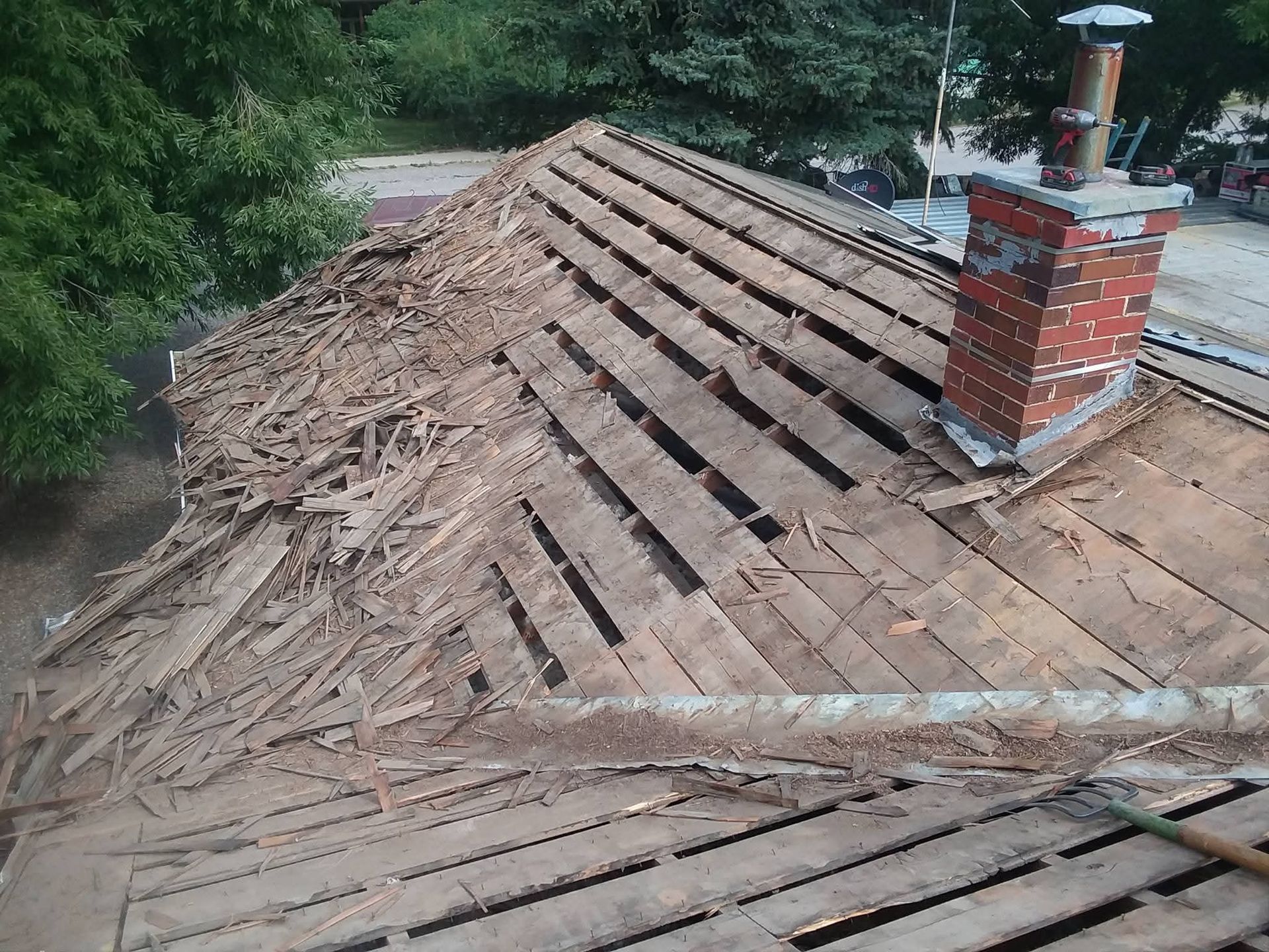 Partially demolished rooftop with exposed wooden planks and a brick chimney.