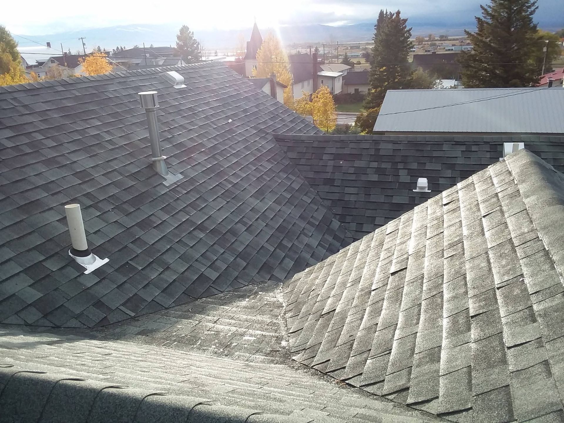 Gray shingle roofs of houses with ventilation pipes against a bright sky.