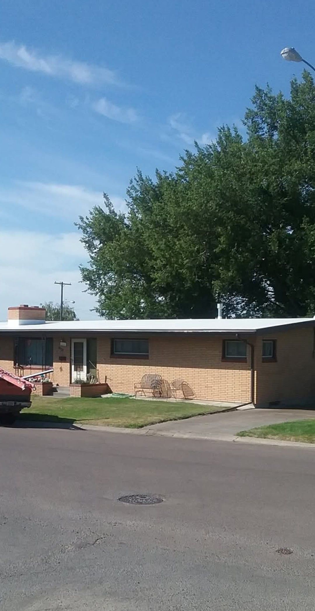 Low-slung brick building with white roof, small front yard, tree, and blue sky.