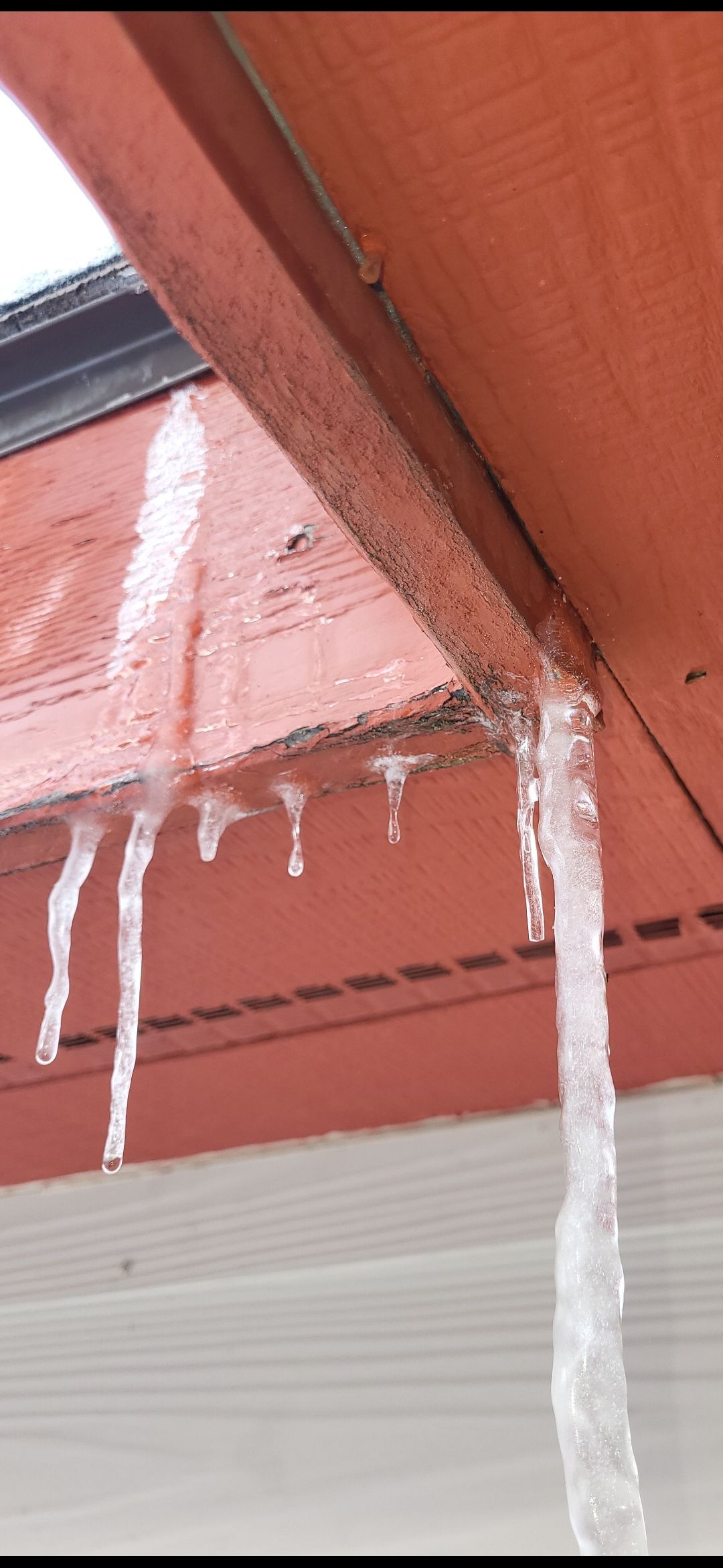 Icicles hanging from a red-brown roof overhang. Gray siding is visible below the overhang.