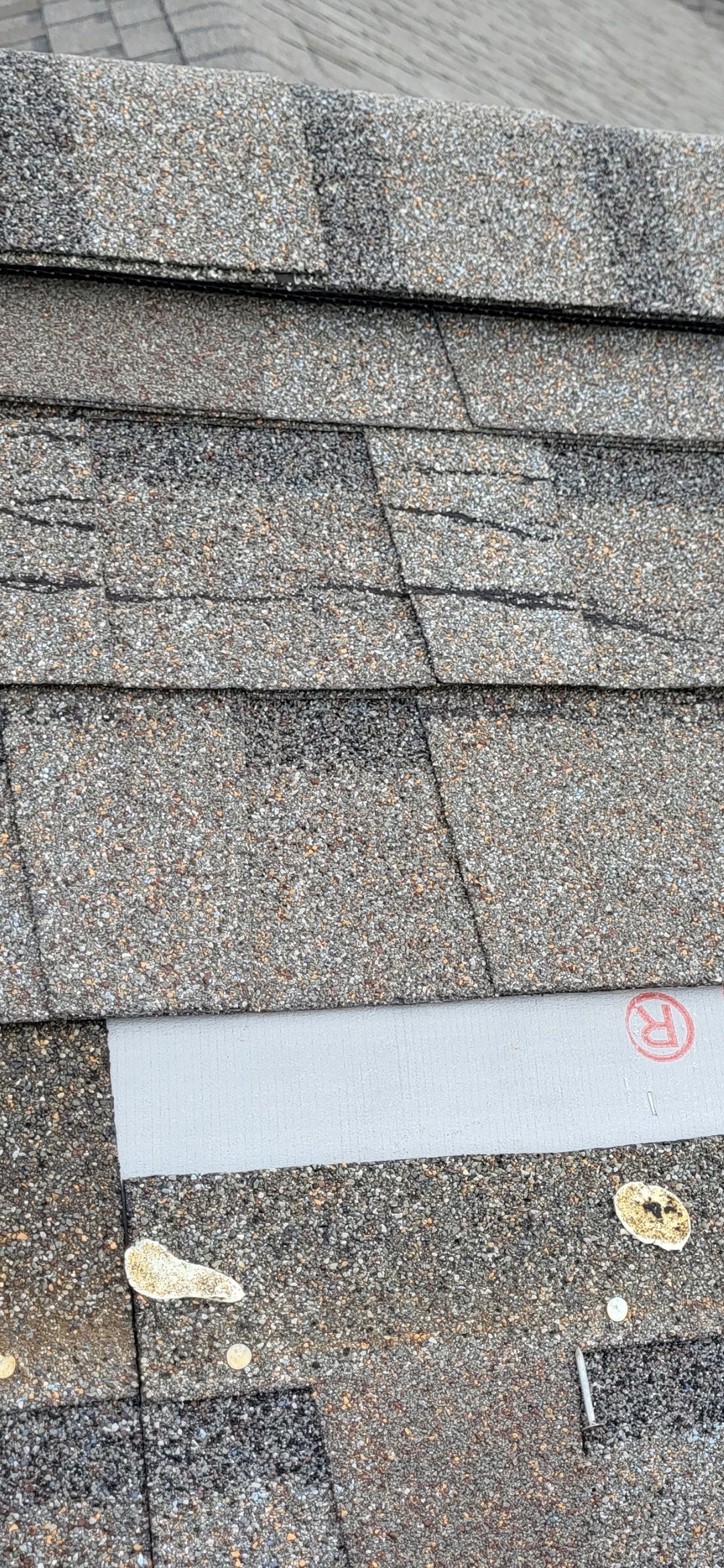 Close-up view of asphalt shingles, with exposed underlayment and debris.
