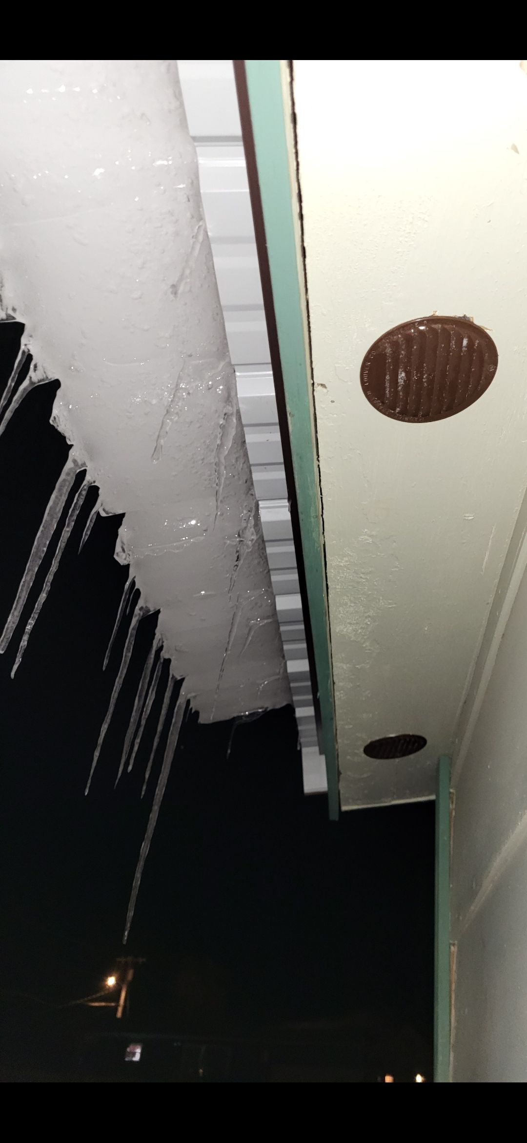 Ice melting from a roof overhang at night, with dark sky and a light source visible.