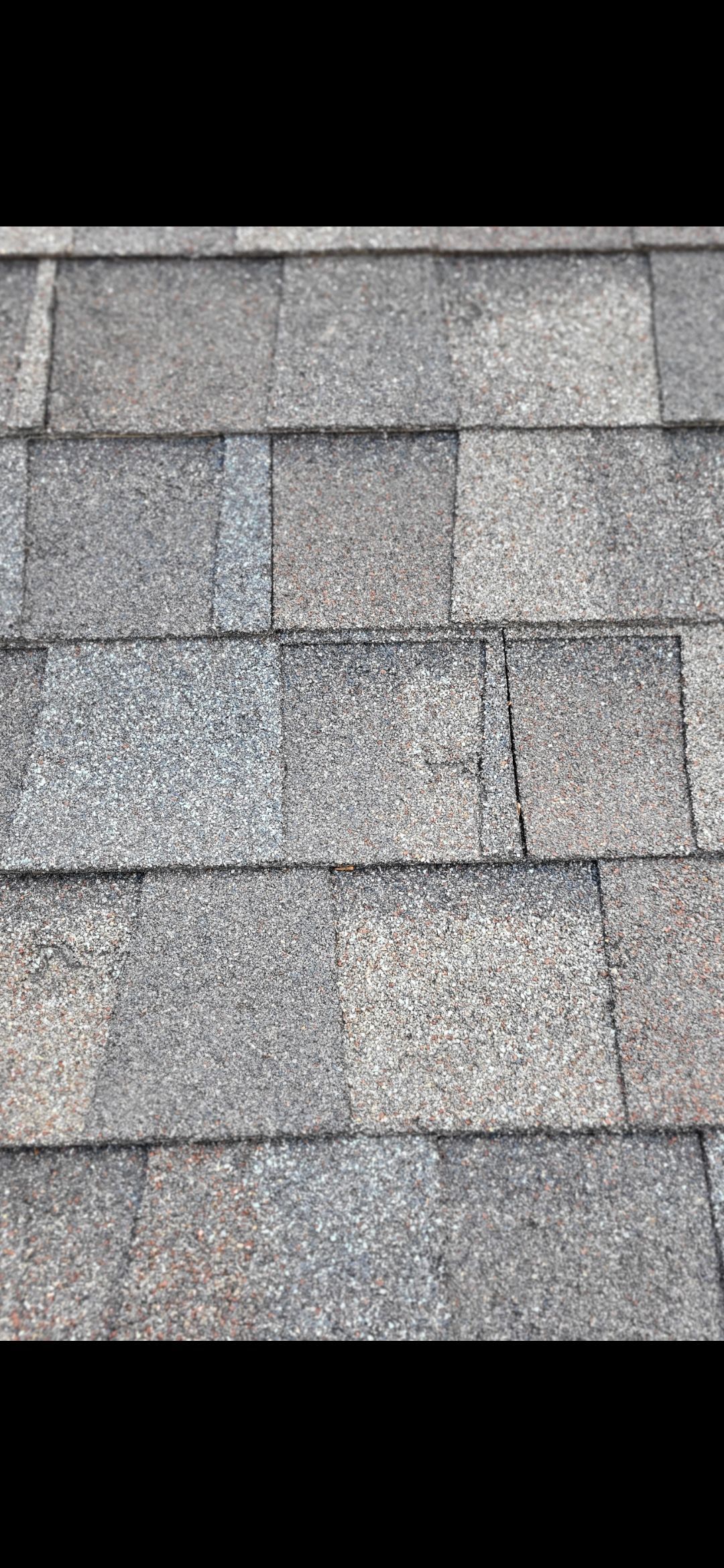 Close-up of weathered gray asphalt roof shingles with some visible damage and wear.