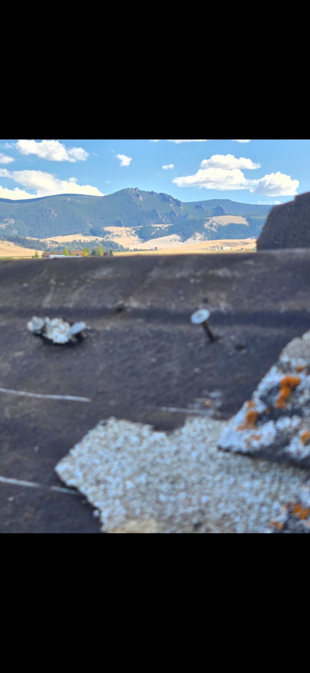 View of mountains with a dark, textured surface in the foreground, possibly a roof. Bright sky.