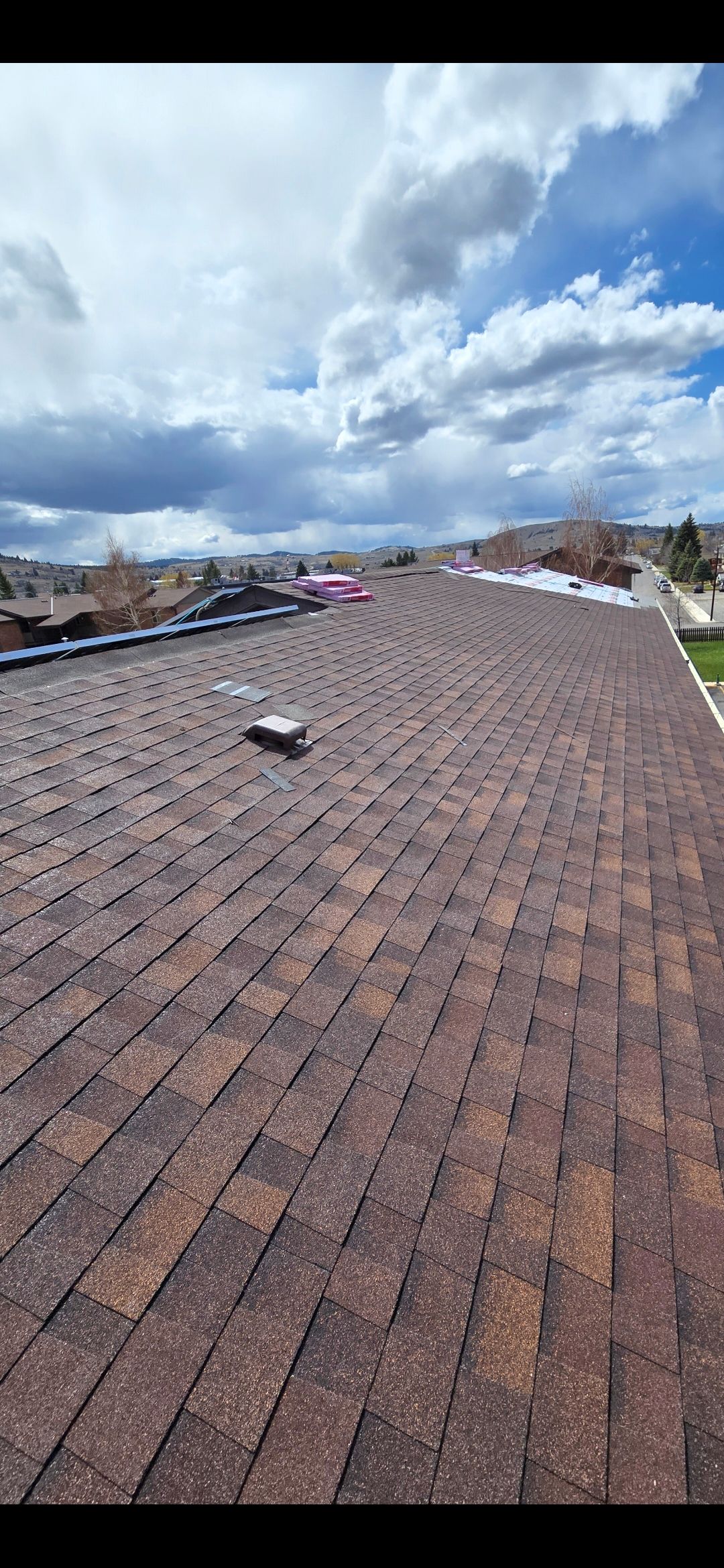 View of a shingled roof under a cloudy blue sky. A vent is visible on the roof.