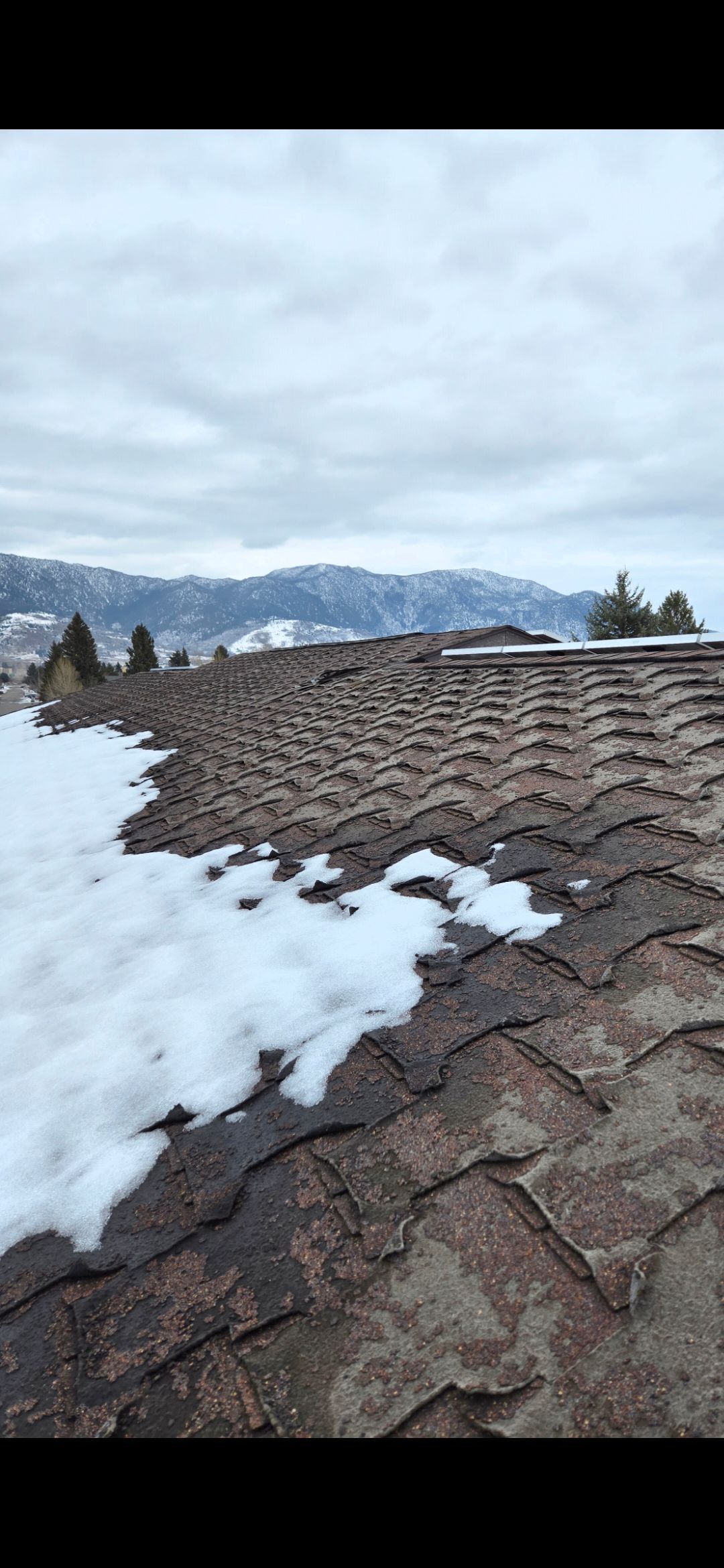 Snow-covered roof with a view of mountains under a cloudy sky.