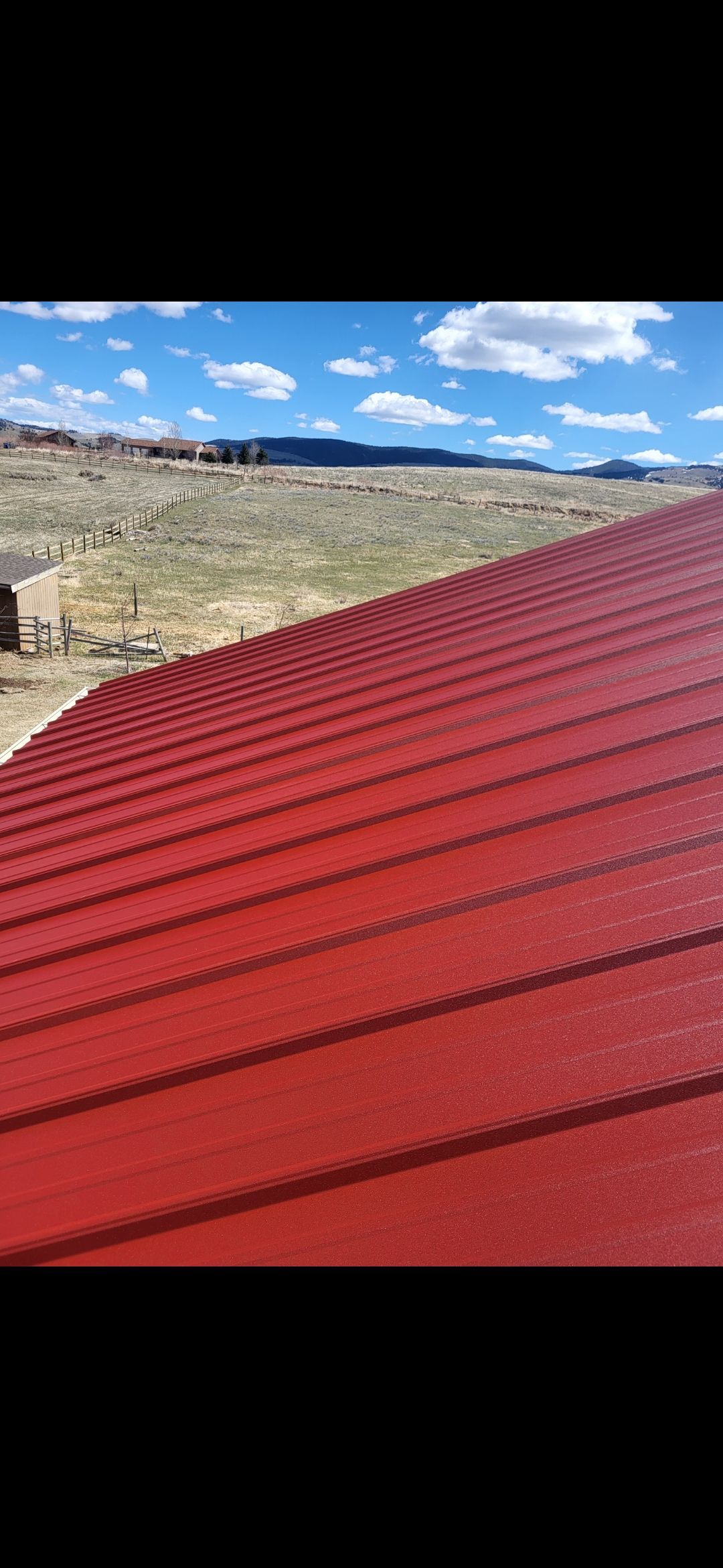 Red corrugated metal roof against a blue sky with clouds, and a landscape background.
