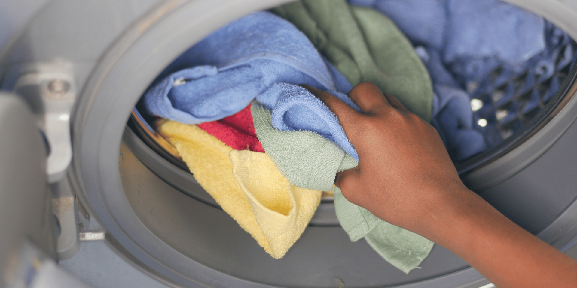 Person's hand reaching into a washing machine filled with colorful clothes.