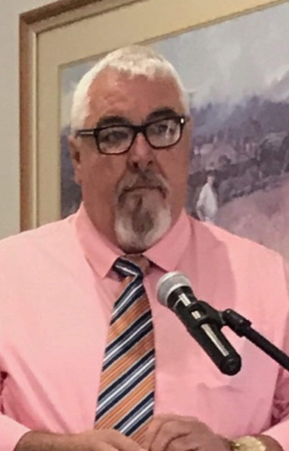A man in a pink shirt and tie is speaking into a microphone