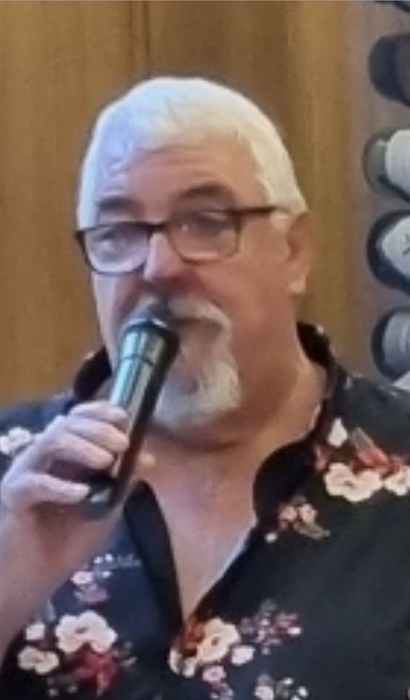 A man with glasses and a beard is singing into a microphone.