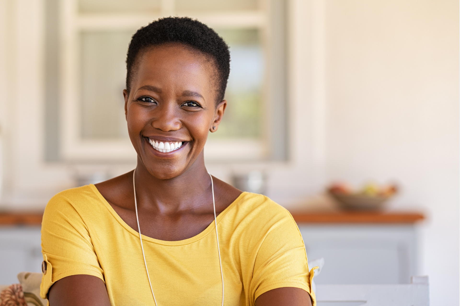 A woman in a yellow shirt is smiling for the camera while sitting at a table.