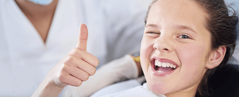 una bambina con il pollice in su e mentre fa l’occhiolino durante una visita dentistica