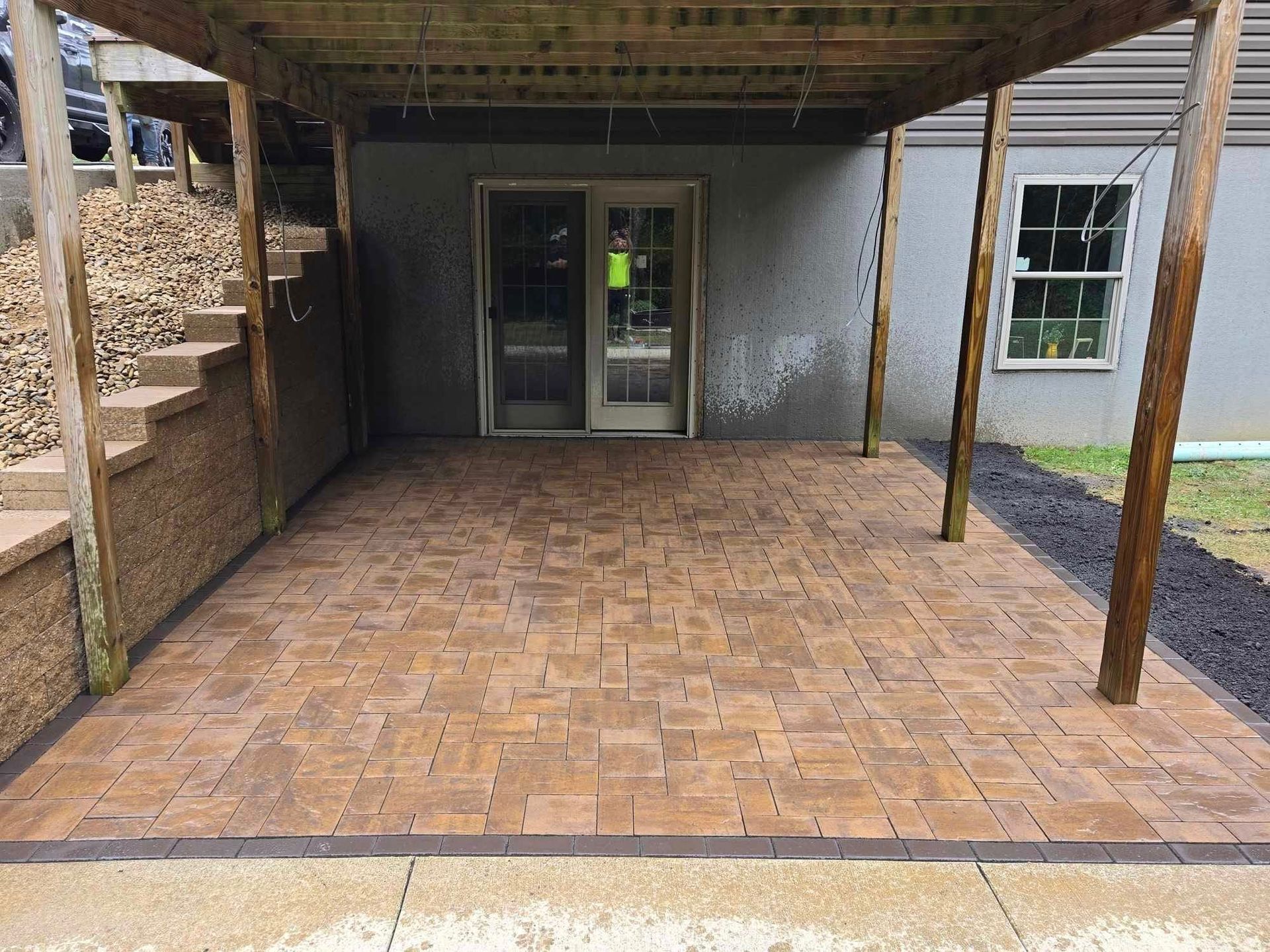 A brick patio with a wooden roof and stairs leading to a house.