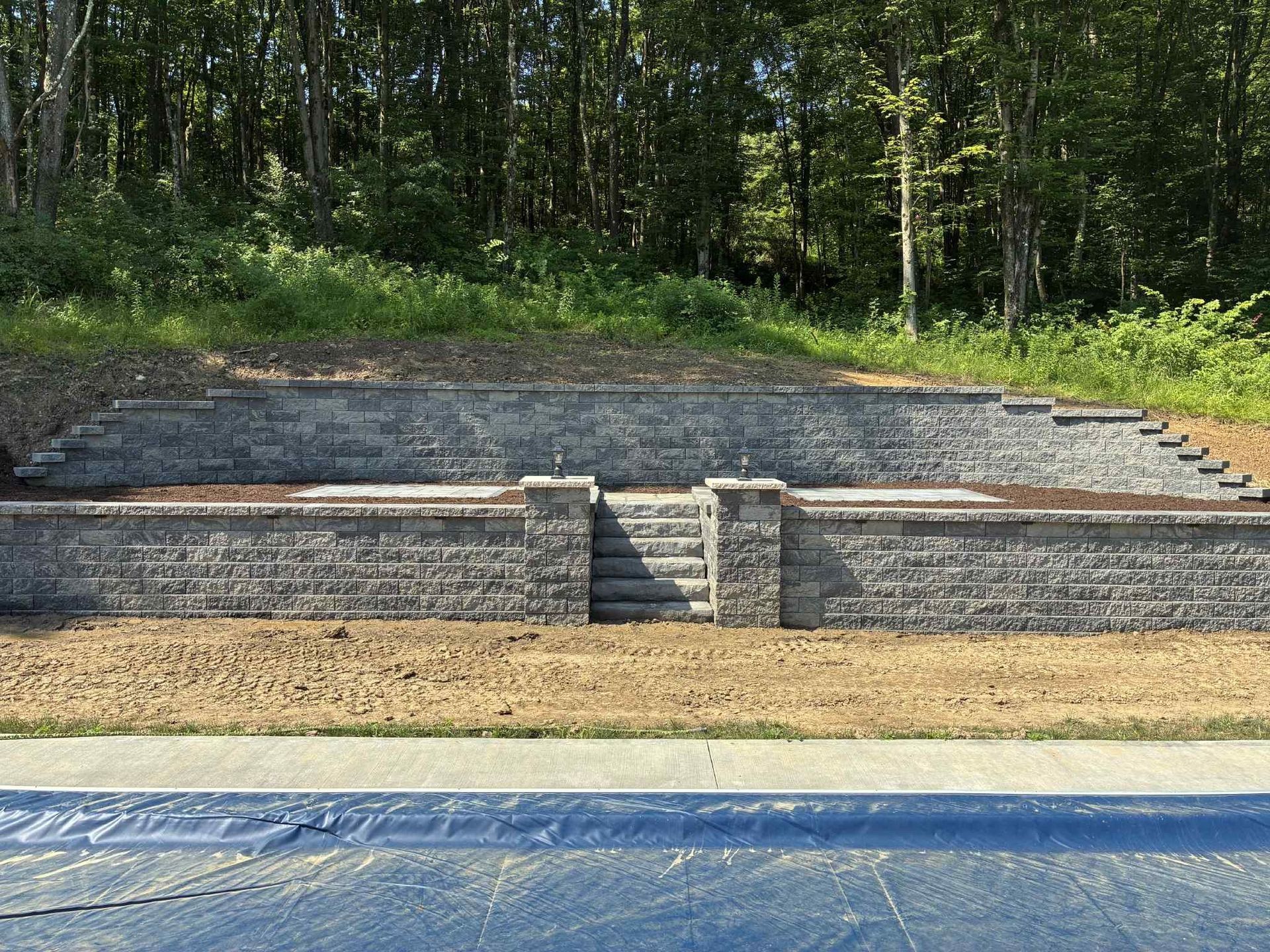 A large brick wall with stairs leading up to it is surrounded by trees.
