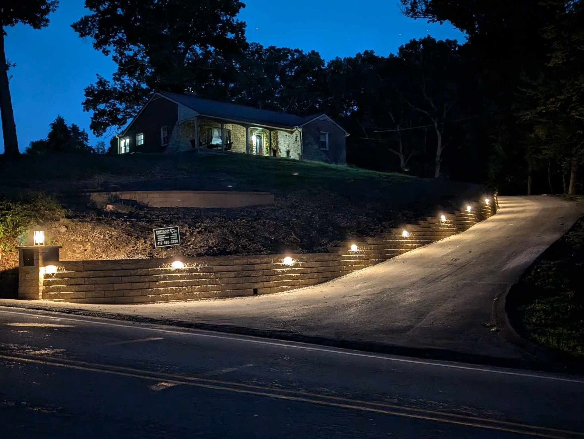 A house is sitting on top of a hill next to a road at night.