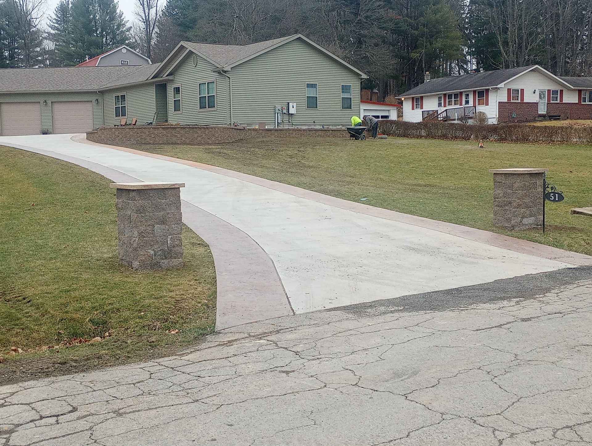 A driveway leading to a house with a green house in the background
