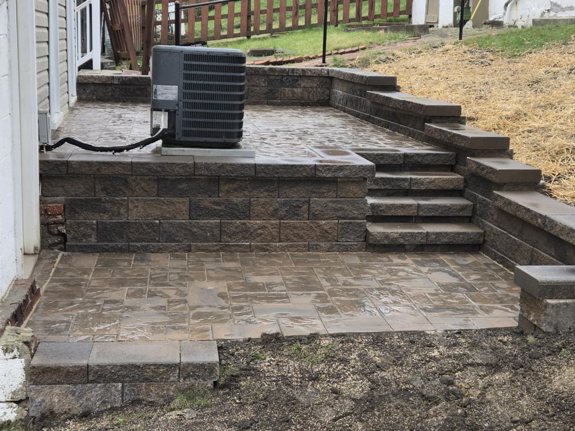 A patio with a wall and stairs and an air conditioner on it.