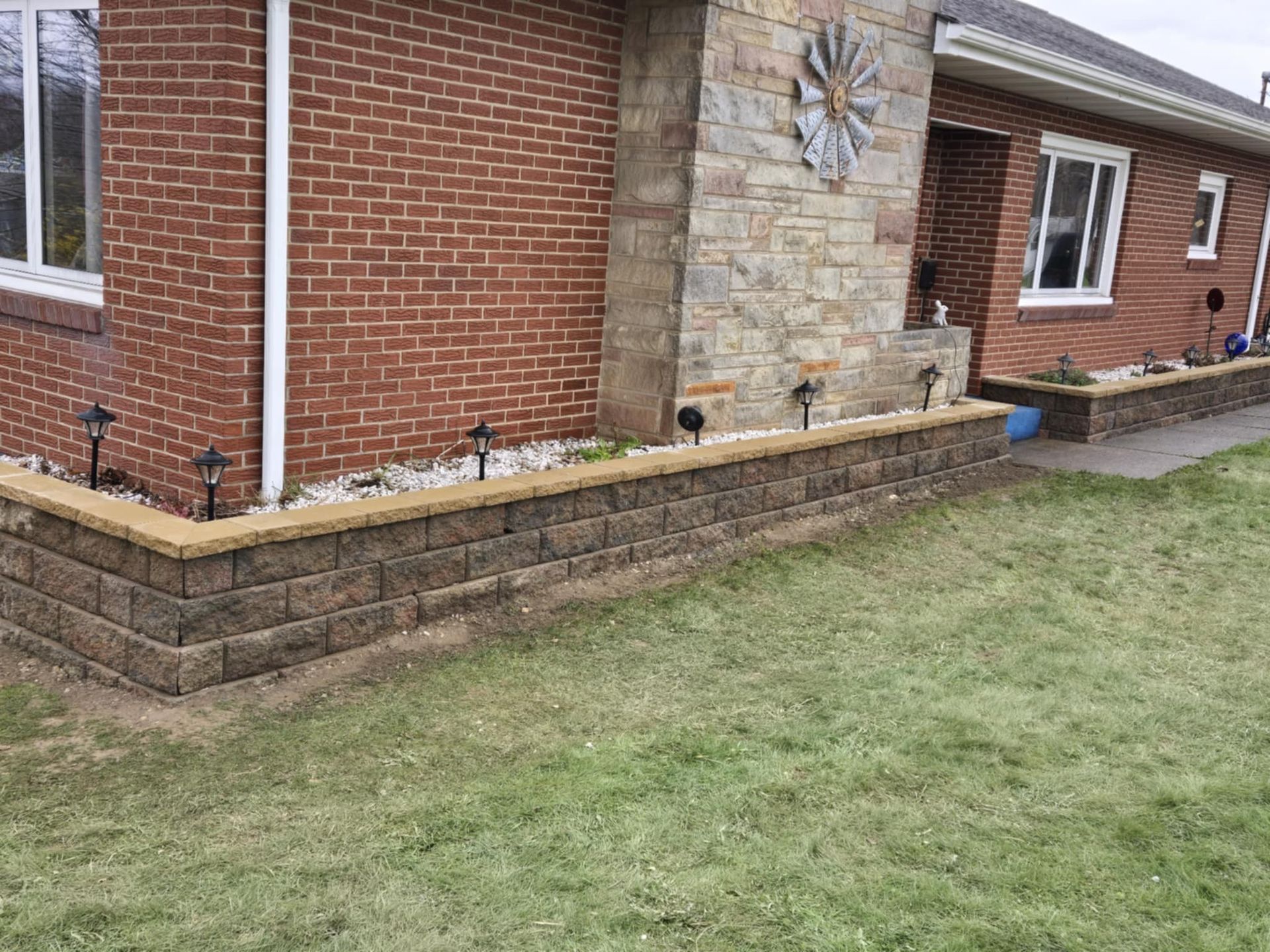 A brick house with a stone wall and a clock on the side of it.