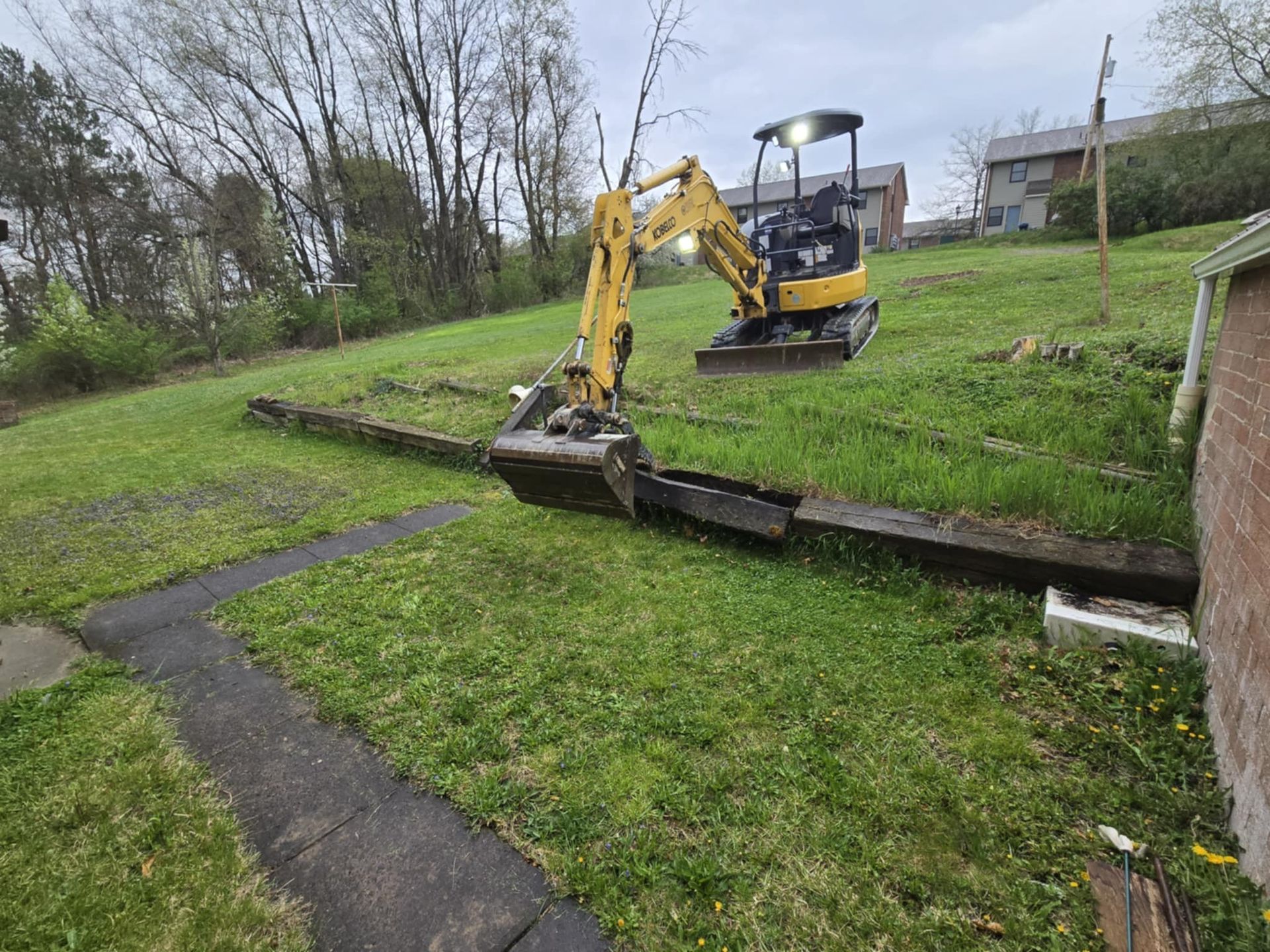 A small yellow excavator is sitting on top of a lush green field.