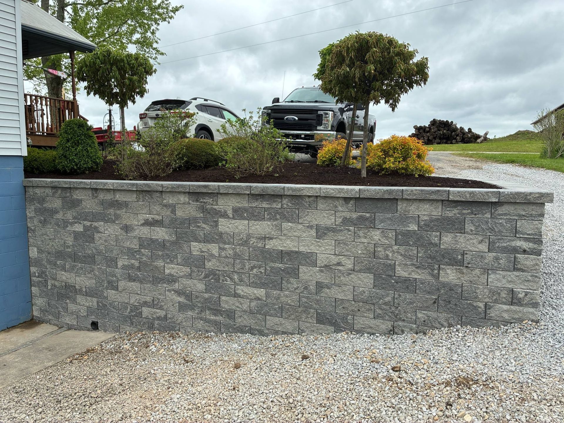 A brick wall surrounds a gravel driveway in front of a house.