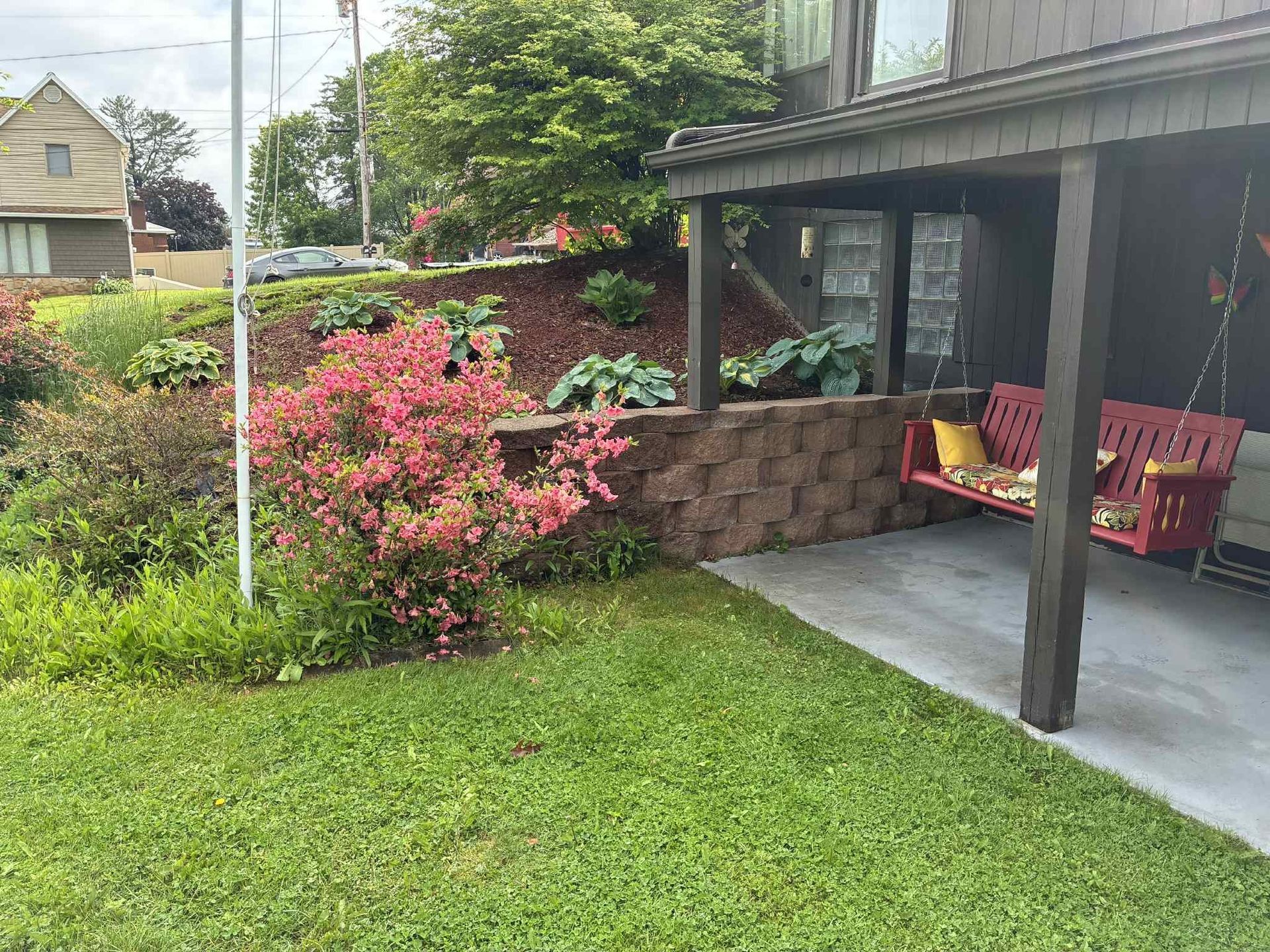 A porch with a red swing and flowers in front of a house.