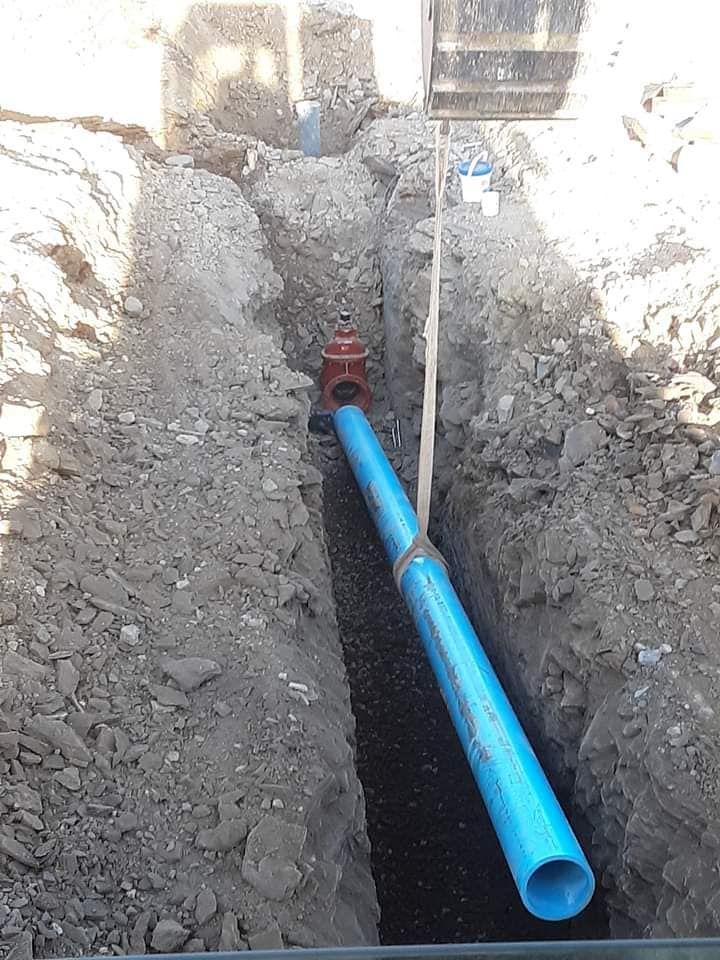 A blue pipe is being installed in a trench.