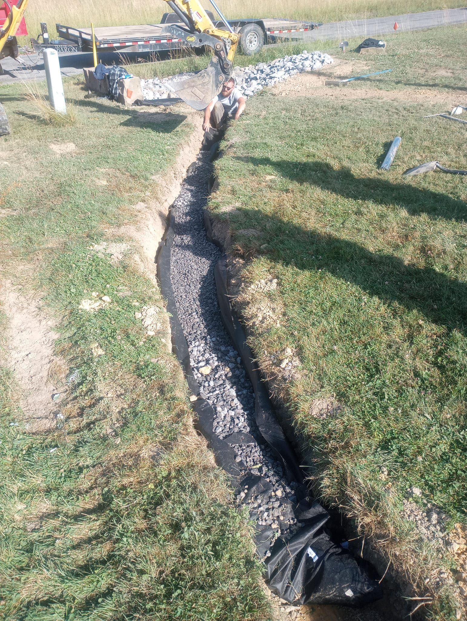 A drain pipe is being installed in a grassy area.
