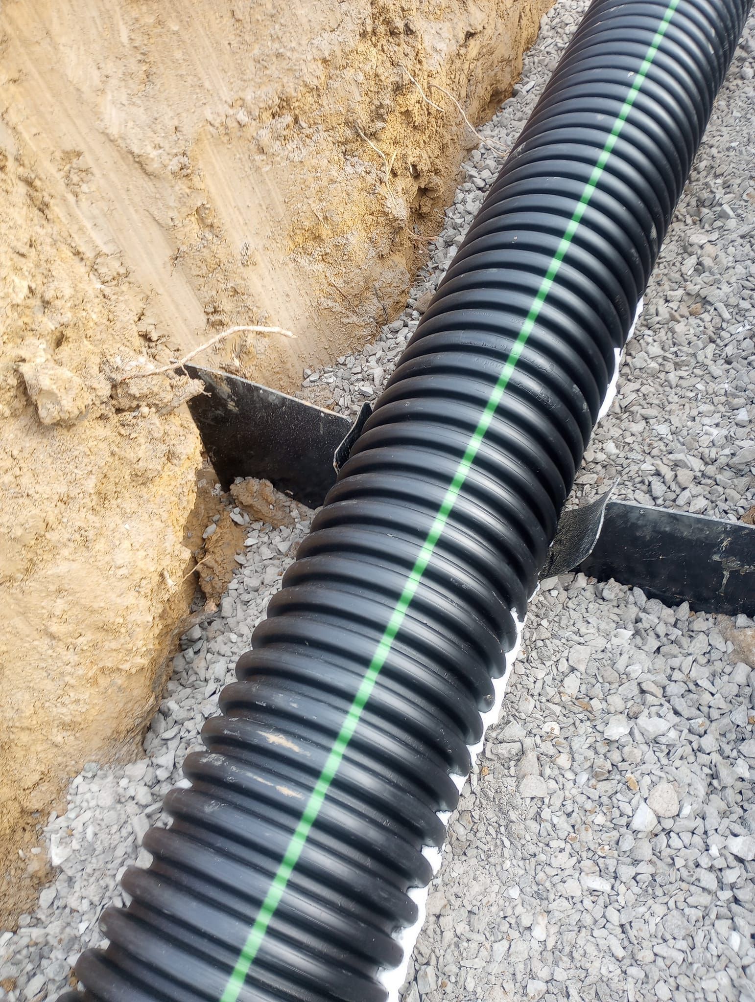 A black pipe with a green stripe on it is laying in the dirt.