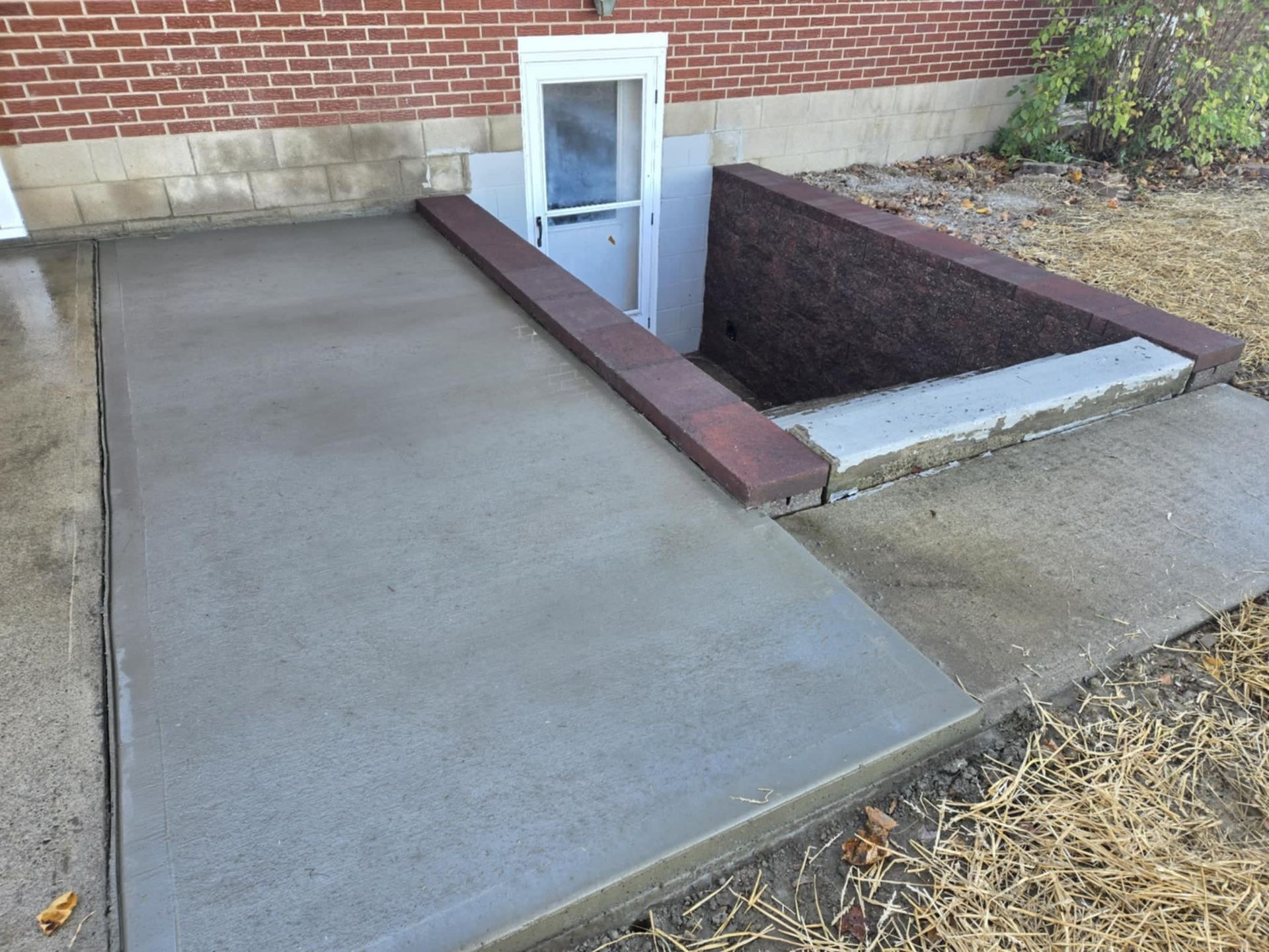 A concrete walkway leading to a window in a basement