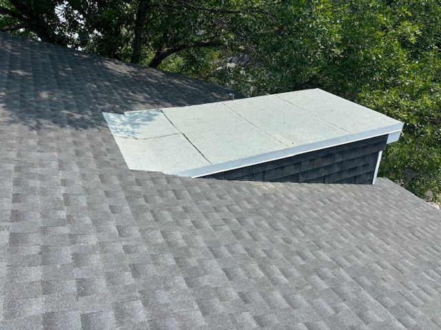 Un toit avec une cheminée au-dessus et des arbres en arrière-plan.