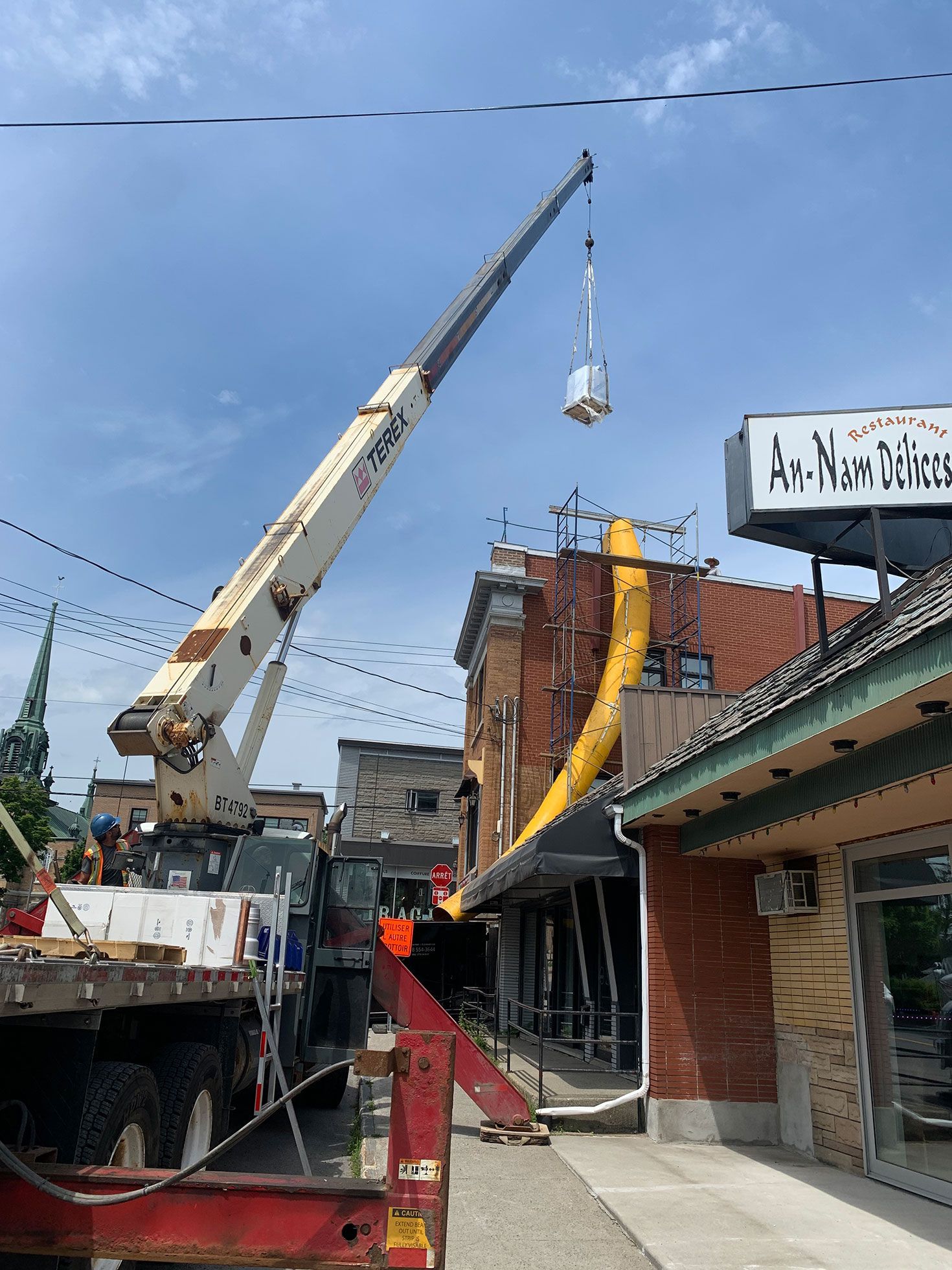 Une grande grue soulève un gros objet du toit d'un bâtiment.