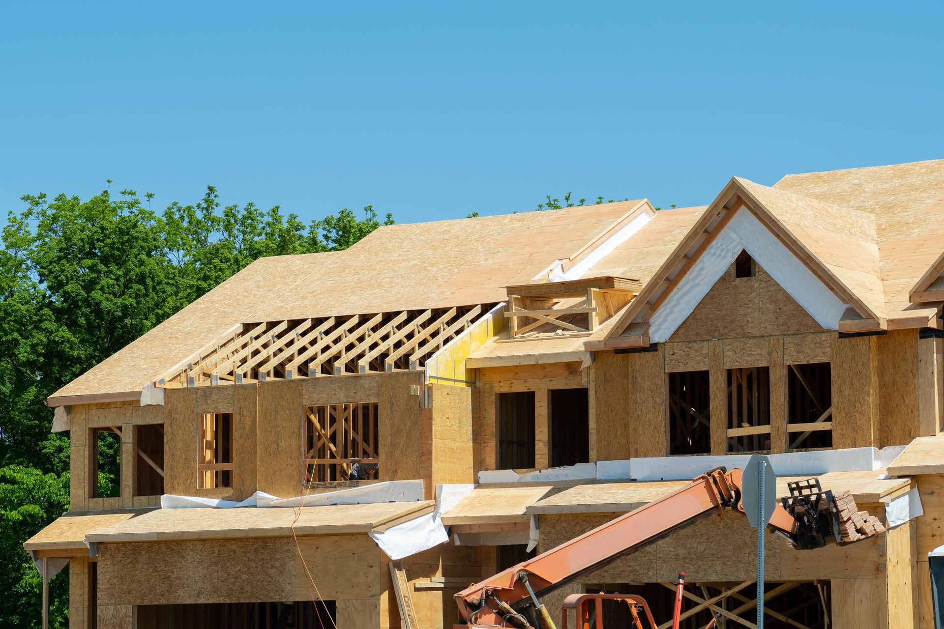 Construction of a two-story wooden house with roof beams exposed and a blue sky in the background.