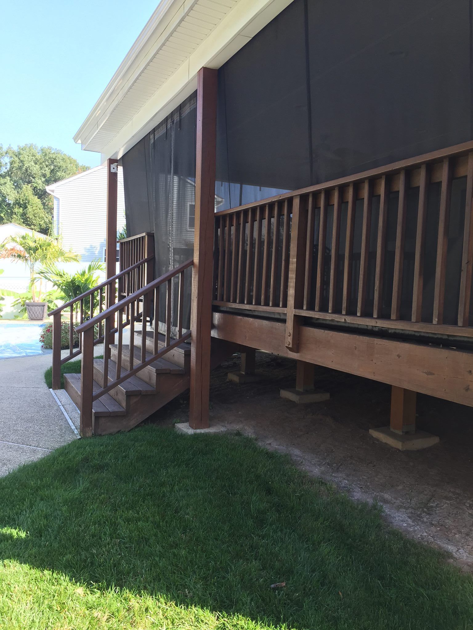 Wooden deck with railing, steps, and screen porch on a sunny day. Green grass in foreground.