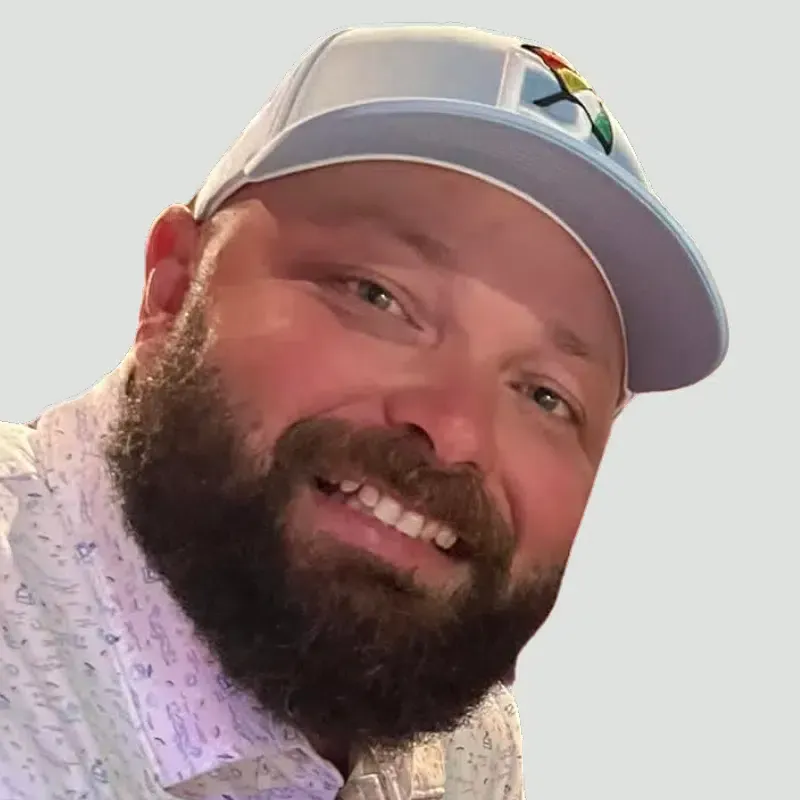 A man with a beard is wearing a hat and smiling.